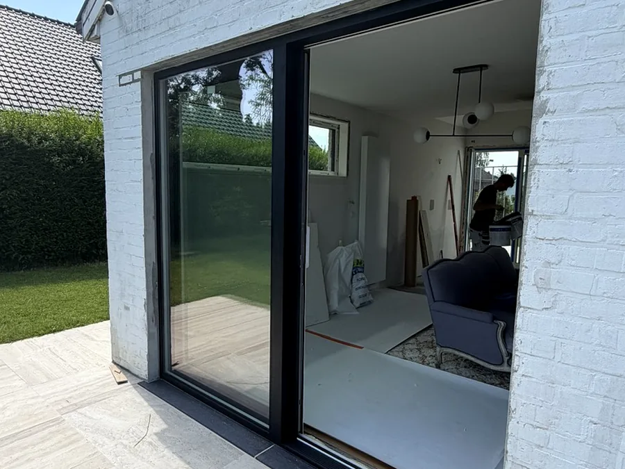 Baie coulissante à profilé noir sur une maison en briques peintes en blanc, ouvrant sur le jardin — réalisation Pulsar Windows