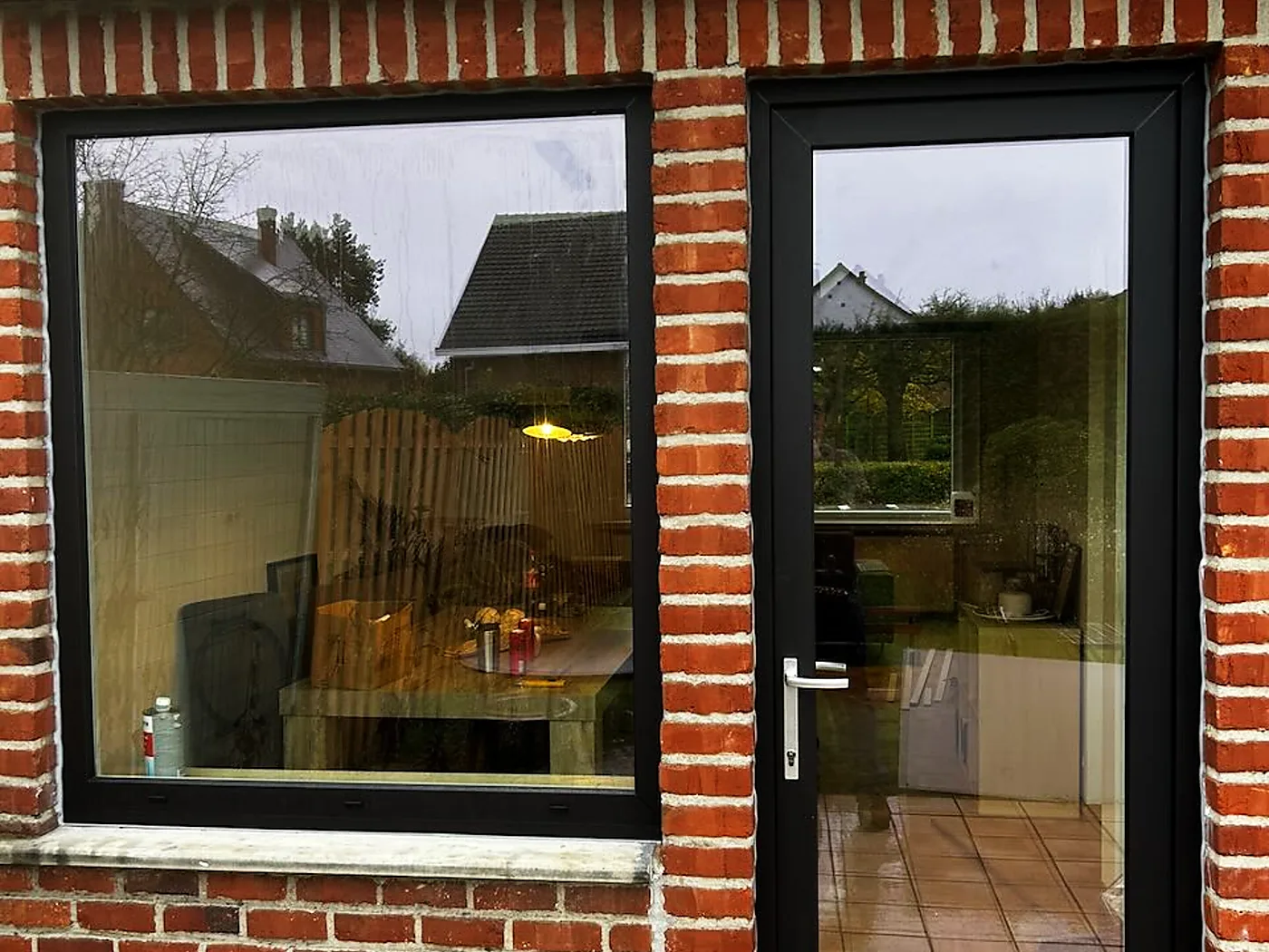 Grande fenêtre à profilé noir sur une façade en briques rouges, ouvrant sur une cuisine chaleureuse — réalisation Pulsar Windows