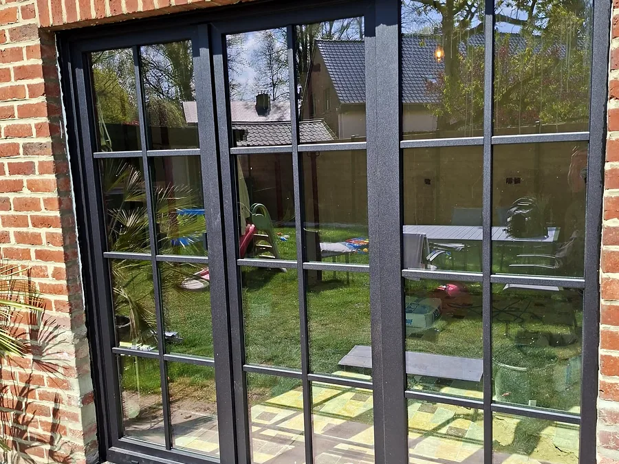Ensemble de fenêtres à profilé noir et petits bois donnant sur un jardin arboré — réalisation Pulsar Windows
