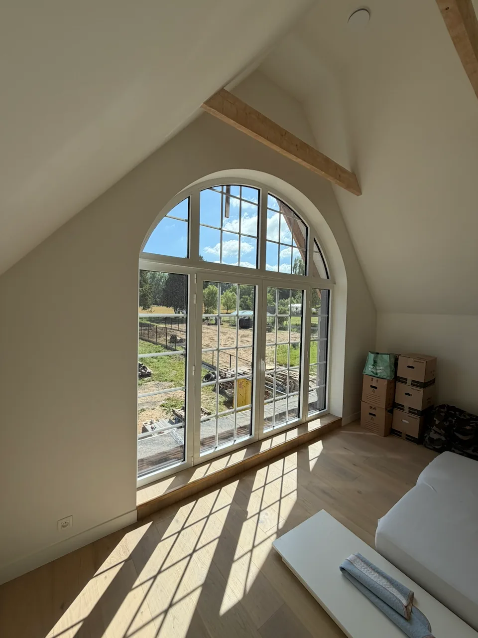 Châssis PVC Kömmerling : grande fenêtre cintrée blanche avec petits bois donnant sur un jardin.