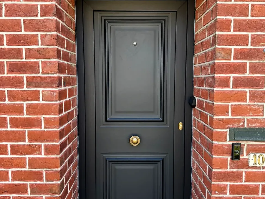 Porte d’entrée anthracite à panneaux moulurés et bouton en laiton, encadrée d’une arche en briques rouges — réalisation Pulsar Windows