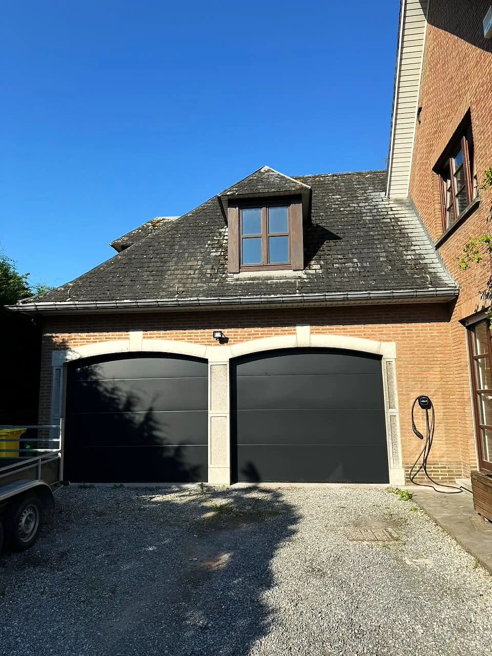 Double porte de garage sectionnelle anthracite sur une maison en briques, avec lucarne — réalisation Pulsar Windows