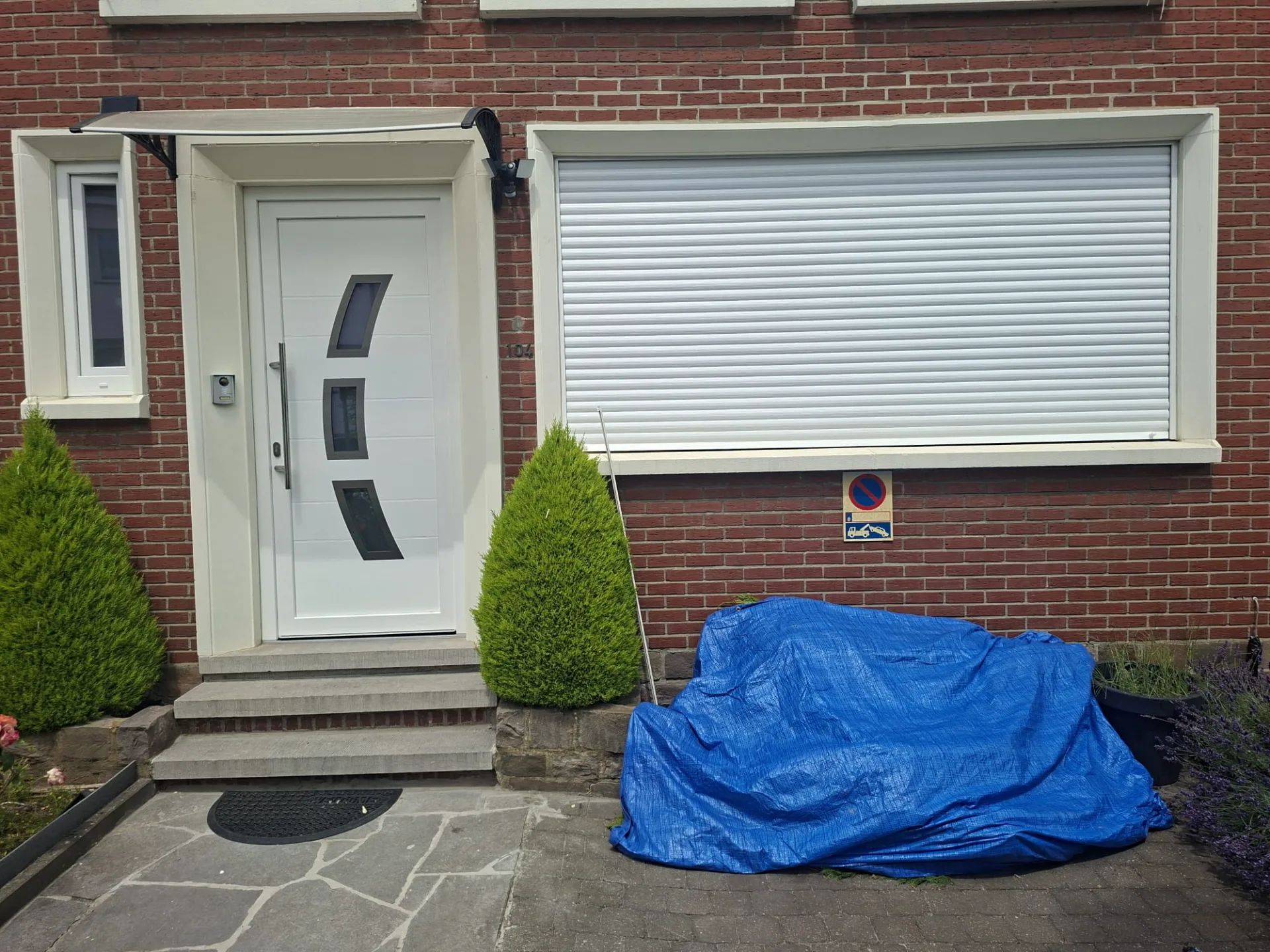 Façade avant : porte d’entrée PVC blanche et fenêtre avec volet roulant descendu