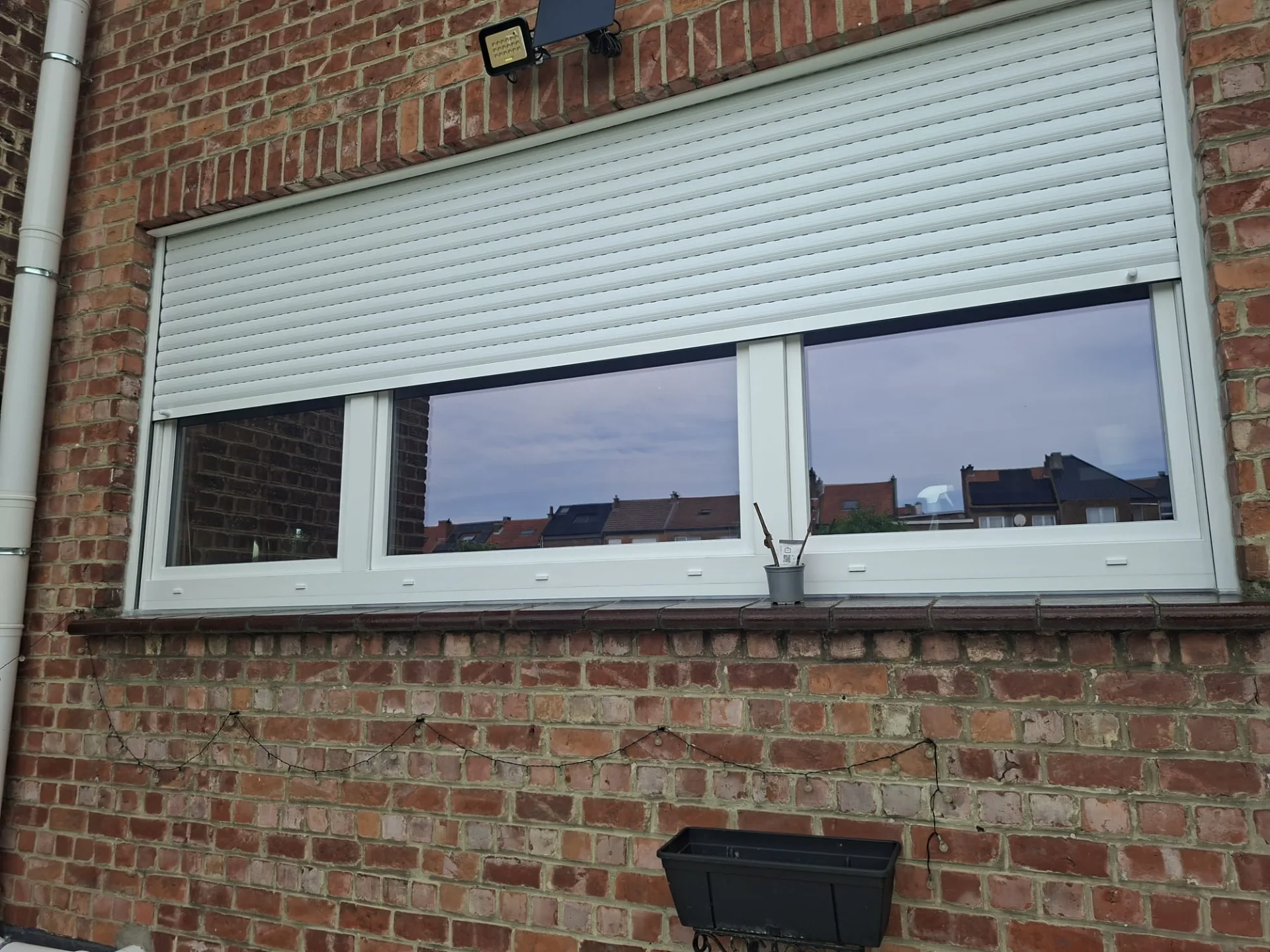 Fenêtre PVC blanche à deux vantaux avec volet roulant à mini-caisson blanc, façade arrière en briques